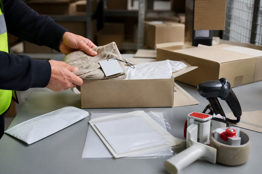 A warehouse worker checking a returned ecommerce parcel beside neutral return documents and a scanner