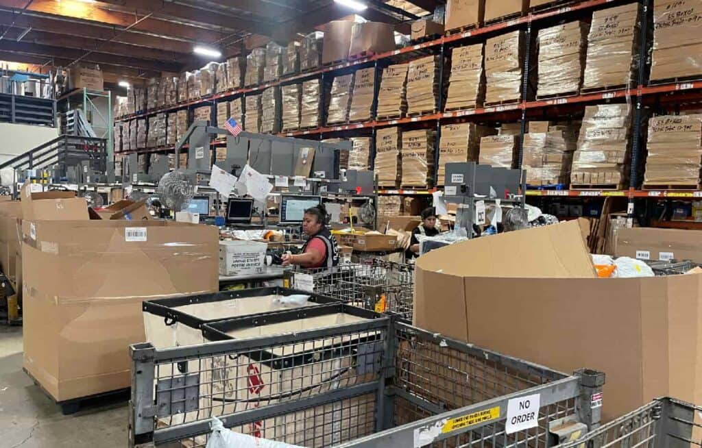 Warehouse staff handling orders among cartons, workstations and storage racks