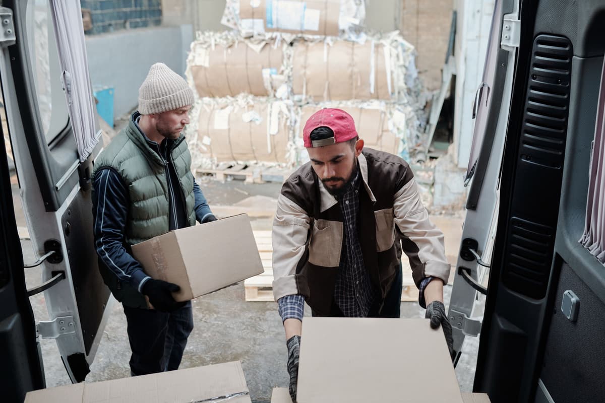Workers moving cartons between a loading area and a van